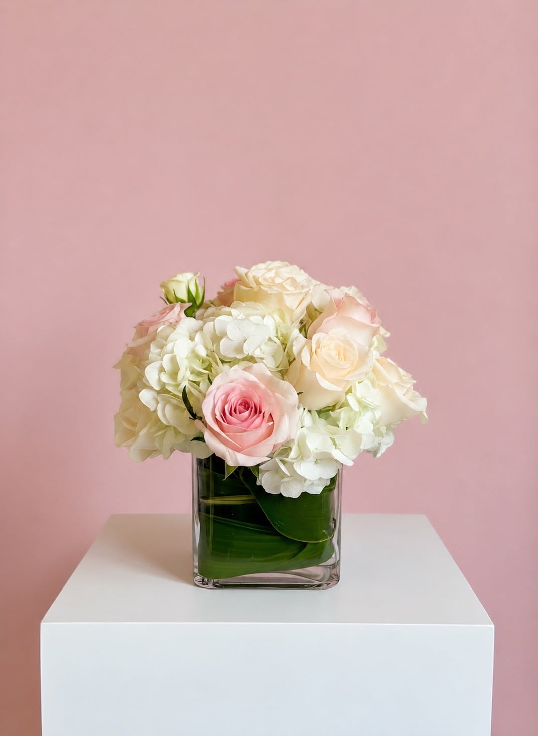 The Glass Cube — White hydrangea, pale pink and cream roses, banana-leaf liner.
