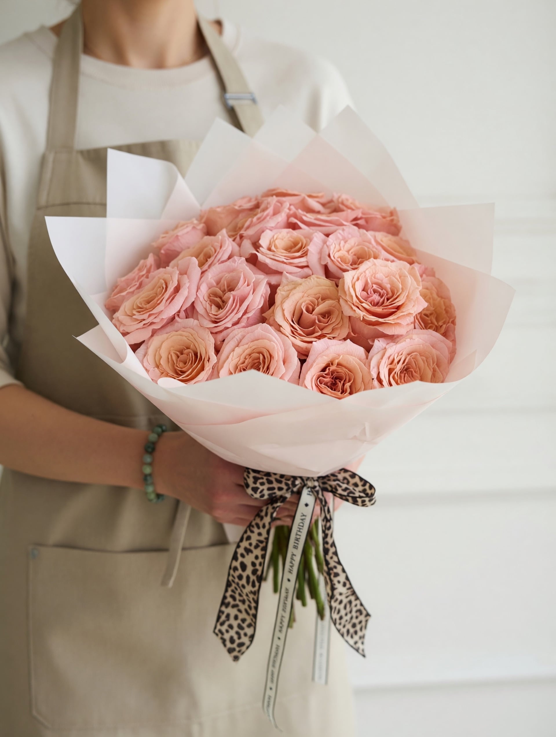 Hand-tied peach garden roses wrapped in pale paper with a printed ribbon — the bouquet in the studio
